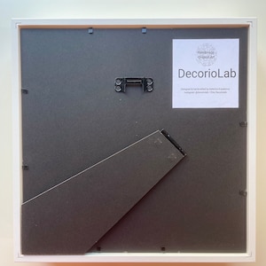 May include: White picture frame with a black mount and a white backing board. The frame has a hanging wire on the back. The frame is labelled "Handmade Original Art DecorioLab Designed & handcrafted by Katerina Каранена Instagram @decoriolab / Etsy Decorolab"