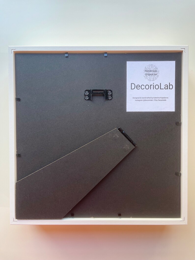 May include: White picture frame with a black mount and a white backing board. The frame has a hanging wire on the back. The frame is labelled "Handmade Original Art DecorioLab Designed & handcrafted by Katerina Каранена Instagram @decoriolab / Etsy Decorolab"