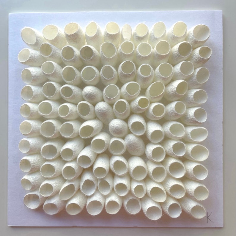 May include: A white square artwork made of numerous white silk cocoons arranged in a grid pattern.
