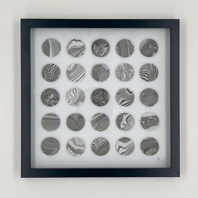 May include: Framed artwork featuring twenty-five circular designs with marbled patterns in shades of gray and white. The artwork is encased in a black frame, creating a modern and minimalist aesthetic. The piece is signed in the bottom right corner.