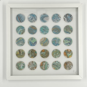 Modern 3D geometric wall art in a white shadow box frame, composed of round wooden dots with one-of-a-kind handmade Suminagashi marbling in blue, aqua, gray, and green, creating a layered abstract display with a calm organic feel. Colorful minimalist art collage.