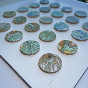 May include: A collection of round, wooden coasters with a swirled, marbled design. The coasters feature shades of teal, orange, yellow, and white. They are arranged on a white surface, creating a visually appealing pattern. The coasters are ideal for home decor.