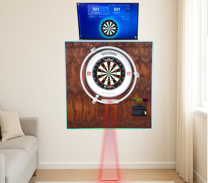 May include: A dartboard with a black, red, and green target is mounted on a wooden backing. A TV displays a dartboard graphic above it. A laser beam projects from the dartboard to the floor. A set of darts is visible.
