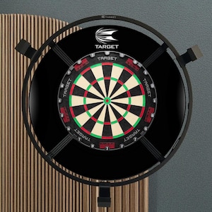 May include: A black dartboard with a red, green, and white target design, surrounded by a black metal frame. The brand name "TARGET" is visible on the board. The dartboard is mounted on a wooden panel.