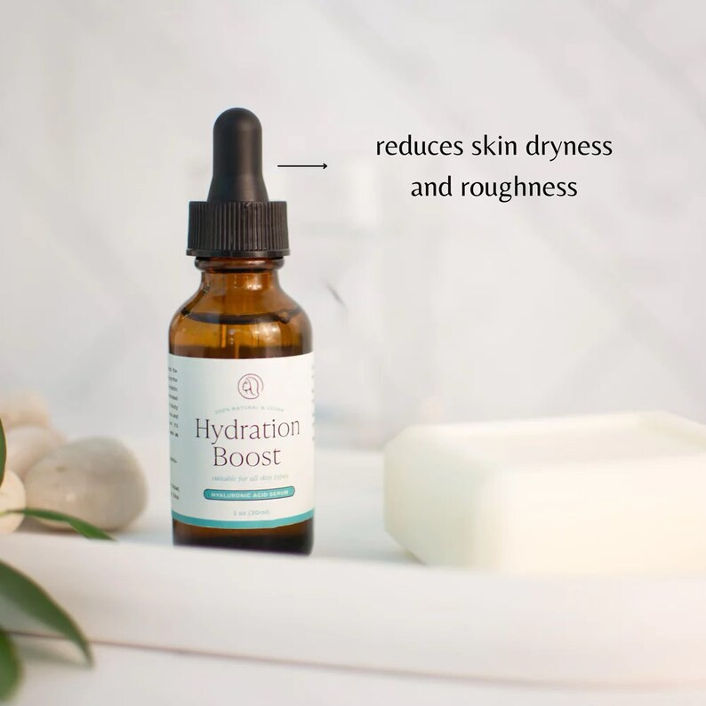 Puede incluir: Un frasco de vidrio marr&oacute;n con un gotero en la parte superior lleno de un l&iacute;quido transparente. El frasco est&aacute; etiquetado con "Hydration Boost Hyaluronic Acid Serum". El frasco est&aacute; sobre una superficie blanca con un objeto rectangular blanco en el fondo. El texto "reduce la sequedad y la aspereza de la piel" est&aacute; escrito en negro sobre un fondo blanco.