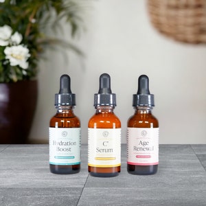 Puede incluir: Tres botellas de vidrio &aacute;mbar con goteros negros y etiquetas blancas. Las etiquetas tienen el texto "Hydration Boost", "C Serum" y "Age Renewal".