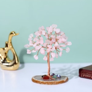 Peut inclure: Un arbre en cristal de quartz rose sur une base en agate brune. L'arbre est fait de fil de fer et possède de nombreux petits cristaux. Il y a également plusieurs petits cristaux à la base de l'arbre.
