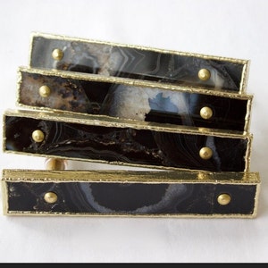 May include: Four black agate drawer pulls with gold trim and accents. The pulls are stacked on top of each other.