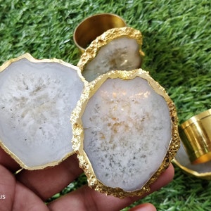 May include: Set of four white agate napkin rings with gold trim. The rings are made of natural agate and have a unique, organic shape. They are perfect for adding a touch of elegance to any table setting.