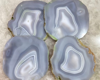 May include: Four agate coasters with a light gray and white banded pattern. The coasters have a natural, rough edge.