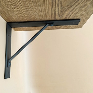 May include: Black metal shelf bracket with a decorative arm. The bracket is attached to a wooden shelf.