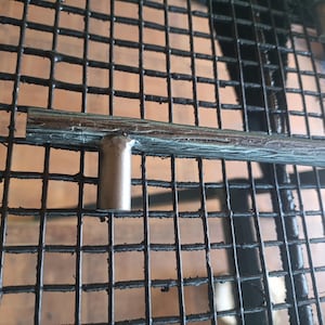 May include: A horizontal metal cabinet pull handle with a textured, bark-like surface finish in a dark gray tone. The handle features a single cylindrical mounting post extending downward from the center of the elongated, rod-shaped bar.