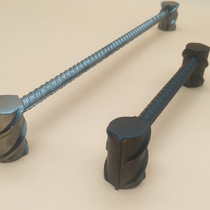 May include: Two metal cabinet pulls with a rebar design. The pulls have a textured, ridged bar and square, twisted end pieces. One pull is longer than the other. The metal has a dark, bluish-gray finish.