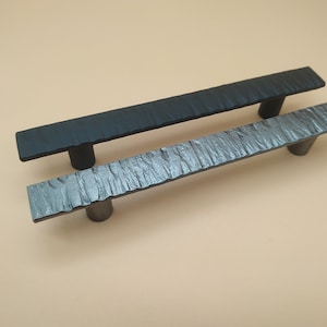 Può includere: Due maniglie per armadi, una nera e una argentata, con una finitura testurizzata. Le maniglie sono in metallo e hanno una forma rettangolare.