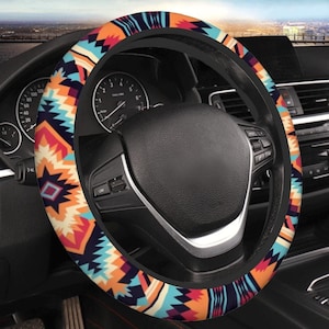 May include: Steering wheel cover with a colorful geometric pattern in shades of orange, blue, and red. The cover is wrapped around a black steering wheel, with the car's dashboard and gauges visible in the background.