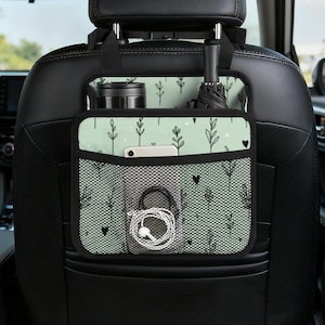 以下が含まれることがあります： 複数のポケットとコンパートメントを備えたカーシートオーガナイザー。オーガナイザーは黒とミントグリーンで、花柄と黒のメッシュポケットが付いています。タンブラー、傘、電話、その他のアイテムを収納できます。