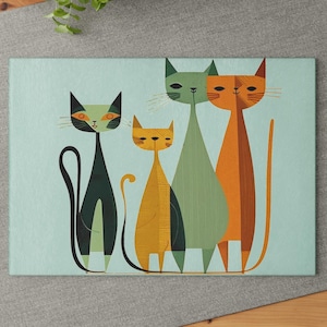 May include: A blue and green kitchen cutting board with a design of four stylized cats. The cats are in a row, with the largest cat in the middle. The cats are all different colors, with one being orange, one being green, one being black, and one being yellow.