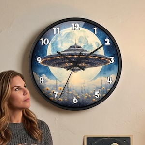 May include: A round wall clock with a black frame features a blue and white illustration of a UFO over a city with a full moon in the background. The clock hands are black. The clock is hanging on a beige wall.
