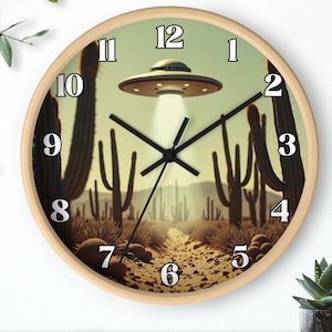 May include: A round wall clock with a beige face and black hands. The clock face features a desert scene with cacti and a flying saucer. The numbers on the clock are in black and white.