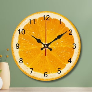 Puede incluir: Un reloj redondo naranja con agujas y números negros. La esfera del reloj es una imagen de una rodaja de naranja con una aguja de segundos roja.