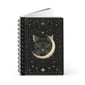 Standing spiral notebook angled slightly to show the black front cover with gold cat and moon design.