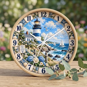 May include: A round wall clock with a light wood frame featuring a coastal scene of a blue and white lighthouse, sailboats on the ocean, and blue hydrangeas. The clock face displays dark blue numbers and a sign that reads Salt Air Happier Here.