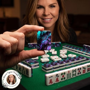 Puede incluir: Primer plano de una ficha de Mahjong con colores turquesa, morado y negro, sostenida por una persona. Otras fichas de Mahjong est&aacute;n sobre una superficie verde. El juego incluye fichas blancas con marcas rojas y verdes.