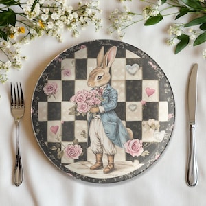 Peut inclure: Une assiette en céramique blanche avec un motif en damier noir et blanc, des roses roses et un lapin tenant un bouquet de roses roses. Le lapin porte une veste bleue et une chemise blanche. L'assiette a une bordure décorative avec des cœurs et des fleurs.