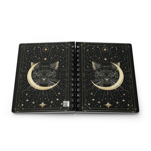 Fully open spiral notebook displaying the front and back covers flat side by side, showing the complete celestial cat design.