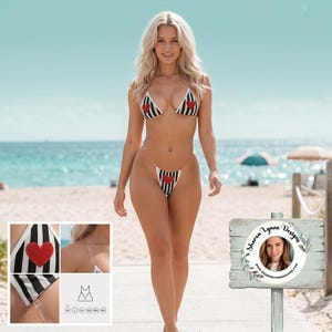 May include: A black and white striped bikini with red heart accents. The bikini top has a triangle design with a red heart on each cup. The bottoms are a thong style with a matching heart. Clear straps are used for the top and bottom.