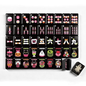 A full 160-piece set of black mahjong tiles with colorful pastel Halloween designs is neatly arranged on a white surface.