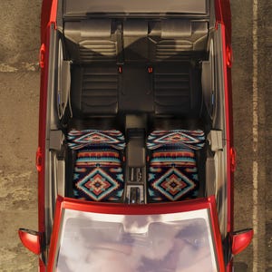 An overhead view of a red car's interior, showing two front seats fitted with colorful geometric patterned seat covers.