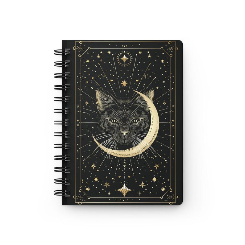 Front cover of a black spiral notebook featuring a gold celestial cat illustration with a crescent moon and stars.
