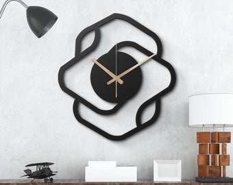 Può includere: Un orologio da parete geometrico nero con lancette dorate e sfondo nero. L'orologio è appeso a una parete bianca sopra un mobile in legno scuro con due scatole bianche in cima.