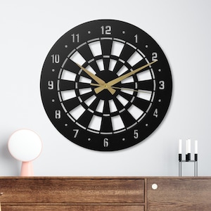 May include: A black and white dartboard clock with gold-colored hands and numbers. The clock is mounted on a white wall above a wooden cabinet. The clock's design resembles a traditional dartboard.
