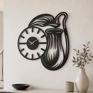 May include: A black wall clock featuring a circular face with minimalist hour markers and gold-colored hands. The clock is integrated into a decorative metal cutout design depicting a pitcher plant with a large leaf and a hanging trap structure.