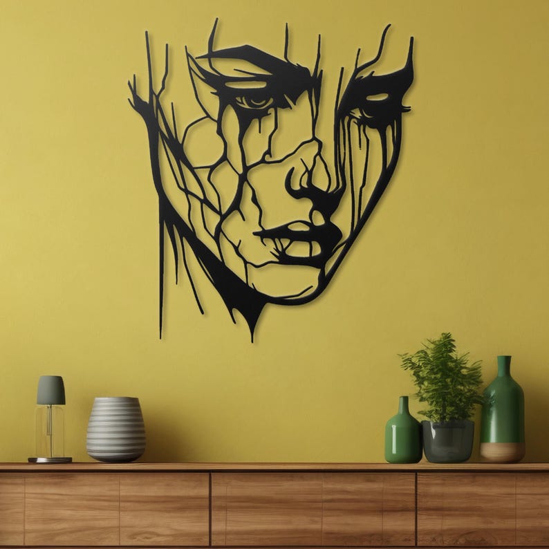 K&ouml;nnte beinhalten: Schwarze Wandkunst aus Metall mit einem stilisierten abstrakten Gesicht mit einem rissigen und abgenutzten Design. Das Gesicht hat einen starken, ausdrucksstarken Blick mit einem leicht nach unten geneigten Mund und geschlossenen Augen.