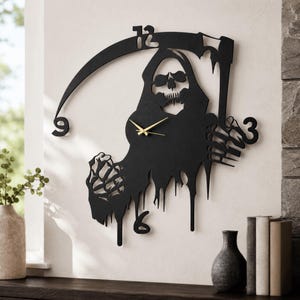 Könnte beinhalten: Eine schwarze Wanduhr mit der Silhouette des Sensenmanns, der eine Sense hält. Das Zifferblatt integriert die Zahlen 3, 6, 9 und 12 in das Design. Sie hat dünne, goldfarbene Stunden- und Minutenzeiger in der Mitte der Figur.