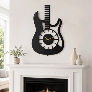 K&ouml;nnte beinhalten: Eine schwarze Wanduhr in Form einer E-Gitarren-Silhouette. Die Uhr verf&uuml;gt &uuml;ber ein zentrales, kreisf&ouml;rmiges Zifferblatt mit wei&szlig;en Stundenmarkierungen, einer soliden schwarzen Mitte und d&uuml;nnen goldfarbenen Zeigern f&uuml;r Stunden, Minuten und Sekunden. Der Gitarrenhals erstreckt sich nach oben mit horizontalen Bundlinien.