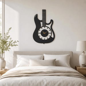 K&ouml;nnte beinhalten: Eine mattschwarze Wanduhr in Form einer E-Gitarren-Silhouette. Das Zifferblatt ist kreisf&ouml;rmig in der Mitte des Gitarrenk&ouml;rpers angebracht und verf&uuml;gt &uuml;ber d&uuml;nne wei&szlig;e Stundenmarkierungen sowie schmale goldfarbene Stunden-, Minuten- und Sekundenzeiger.