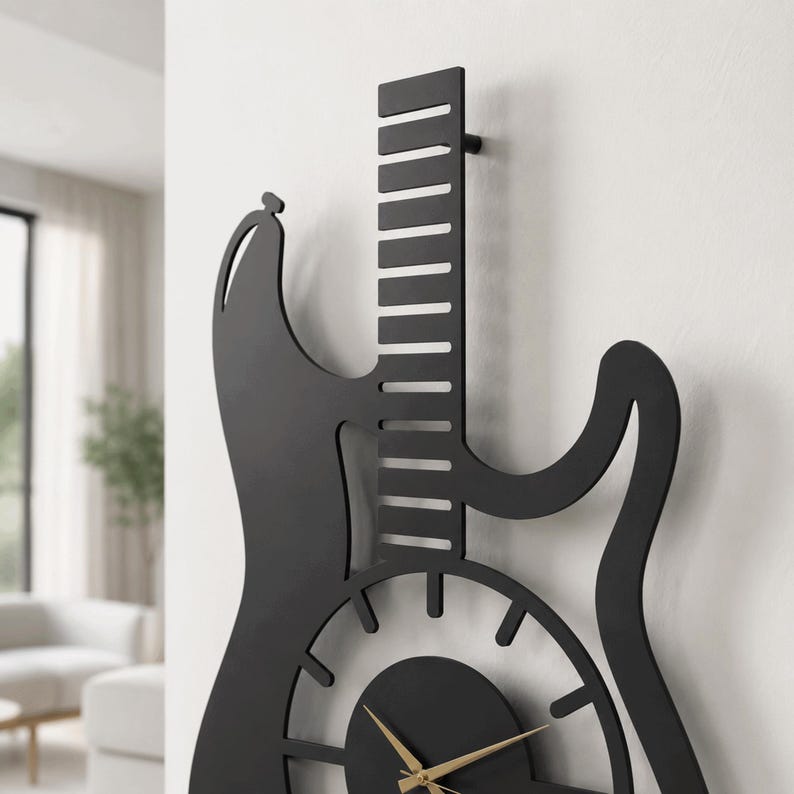 K&ouml;nnte beinhalten: Eine mattschwarze Wanduhr in Form einer E-Gitarren-Silhouette. Die Uhr verf&uuml;gt &uuml;ber einen langen Hals mit horizontalen Ausschnitten, einen kreisf&ouml;rmigen K&ouml;rper mit strahlenf&ouml;rmigen Stundenmarkierungen und d&uuml;nne goldene Zeiger in der Mitte.