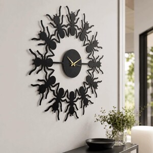 May include: A circular wall clock featuring a black frame composed of multiple ant silhouettes arranged in a ring. The center is a solid black circle with thin, gold-colored hour and minute hands. The design creates a continuous, repeating pattern.