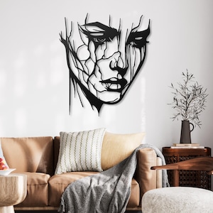 K&ouml;nnte beinhalten: Schwarze Wandkunst aus Metall mit einem stilisierten abstrakten Gesicht mit einem abgenutzten Look. Das Gesicht ist mit einer gezackten Linie umrandet und hat einen tropfenden Effekt.
