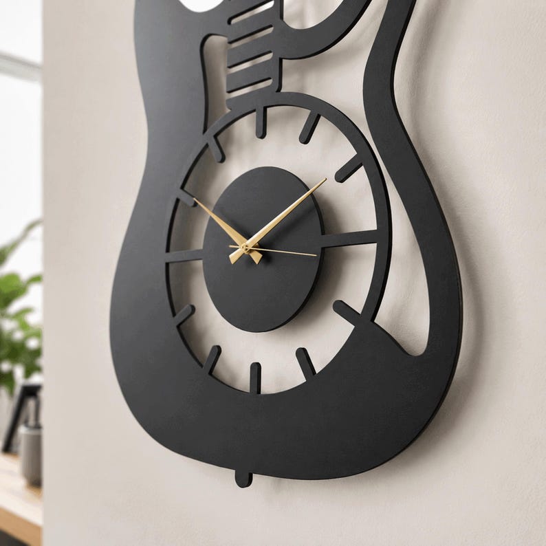 K&ouml;nnte beinhalten: Eine mattschwarze Wanduhr in Form eines E-Gitarrenkorpus. Die Uhr verf&uuml;gt &uuml;ber ein kreisf&ouml;rmiges Zentrum mit d&uuml;nnen, goldfarbenen Zeigern f&uuml;r Stunden, Minuten und Sekunden. Der &auml;u&szlig;ere Rahmen ist eine massive schwarze Silhouette einer Gitarre.