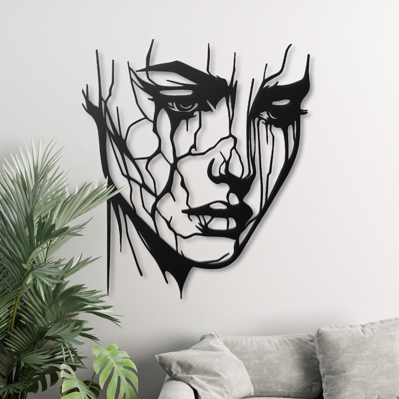K&ouml;nnte beinhalten: Schwarze Wandkunst aus Metall mit einem stilisierten abstrakten Gesicht mit einem verwitterten Look. Das Gesicht ist mit einem gezackten, gebrochenen Linienmuster umrandet.