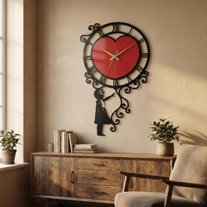 Può includere: Un orologio da parete decorativo con un quadrante a forma di cuore rosso e lancette dorate, circondato da una cornice circolare nera con numeri romani. Una silhouette nera di un bambino indica l'orologio.