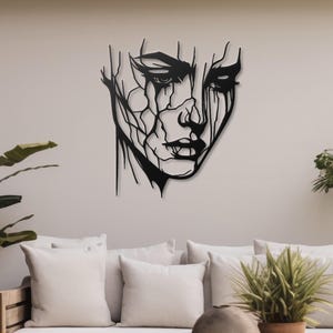 K&ouml;nnte beinhalten: Schwarze Wandkunst aus Metall mit einem stilisierten abstrakten Gesicht mit einem detaillierten Design. Das Gesicht ist schwarz umrandet und hat einen verwitterten Look.
