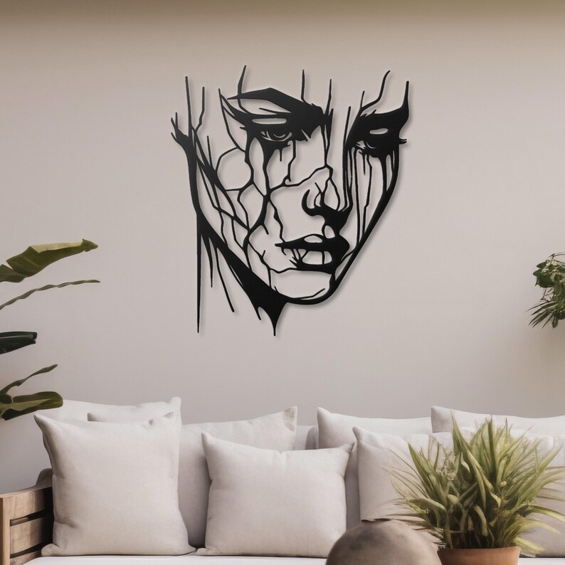 K&ouml;nnte beinhalten: Schwarze Wandkunst aus Metall mit einem stilisierten abstrakten Gesicht mit einem detaillierten Design. Das Gesicht ist schwarz umrandet und hat einen verwitterten Look.