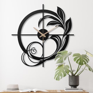 May include: Black metal wall clock with a floral design and gold-colored hands. The clock is circular and has a minimalist design.