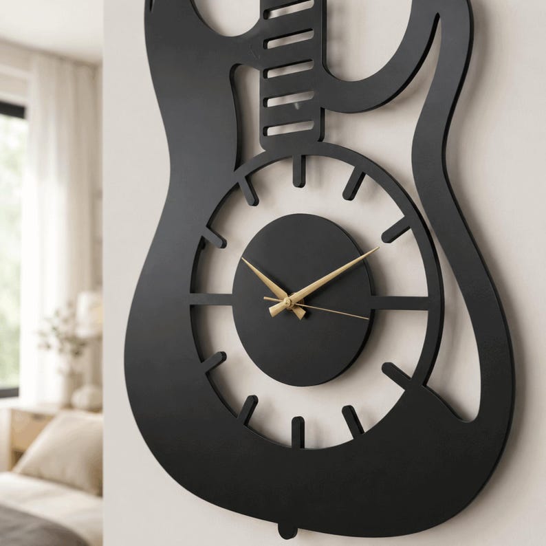 K&ouml;nnte beinhalten: Eine mattschwarze Wanduhr in Form einer E-Gitarren-Silhouette. Die Uhr verf&uuml;gt &uuml;ber ein kreisf&ouml;rmiges Zifferblatt mit zw&ouml;lf gleichm&auml;&szlig;ig verteilten rechteckigen Markierungen und zwei d&uuml;nnen, goldfarbenen Zeigern aus Metall f&uuml;r die Zeitanzeige.